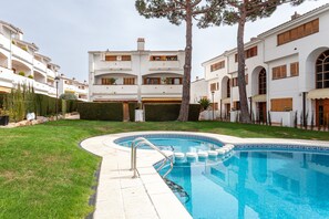 A swimming pool with a tiled deck, surrounded by a well-maintained lawn and a row of white buildings with balconies. - "La Marinera Beach House" with Terraces, Shared Pools & Wi-Fi (Pltja d´Aro)