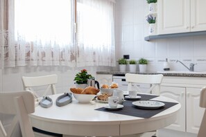A white dining table with a black placemat, white chairs, a bowl of croissants, a coffee pot, and a small potted plant. - "La Marinera Beach House" with Terraces, Shared Pools & Wi-Fi (Pltja d´Aro)
