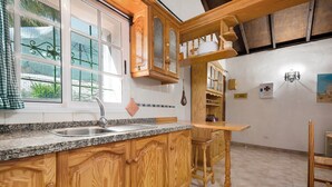 Une cuisine avec des meubles en bois, un plan de travail en granit, un évier et un tabouret de bar.