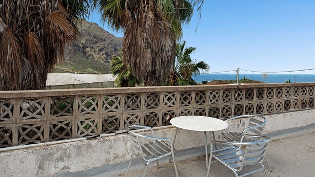 Un balcon avec des chaises et une table en métal, donnant sur une plage et des montagnes.