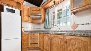 Une cuisine avec des meubles en bois, un réfrigérateur blanc, un plan de travail en granit, une fenêtre avec un rideau à carreaux et un pare-feu en carrelage.