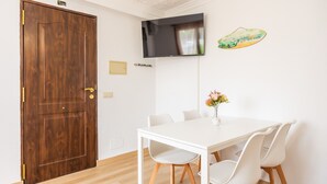 A room with a wooden door, a white table with chairs, a flat-screen TV mounted on the wall, and a small decorative item on the wall. - “Felipe 1-5” Apartment with Terrace, Shared Pool & Wi-Fi (Tourist Taxes Included) (Cala Dor)