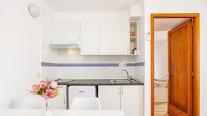 A compact kitchen with white cabinets, a built-in oven, and a sink. A dining table with chairs is positioned in front of the kitchen. - “Felipe 1-5” Apartment with Terrace, Shared Pool & Wi-Fi (Tourist Taxes Included) (Cala Dor)