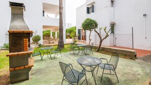 An outdoor patio with a grill, chairs, and tables, surrounded by white buildings. - “Felipe 1-5” Apartment with Terrace, Shared Pool & Wi-Fi (Tourist Taxes Included) (Cala Dor)