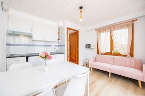 A modern kitchen with white cabinets, a dining table with chairs, a pink sofa, and a wooden door.