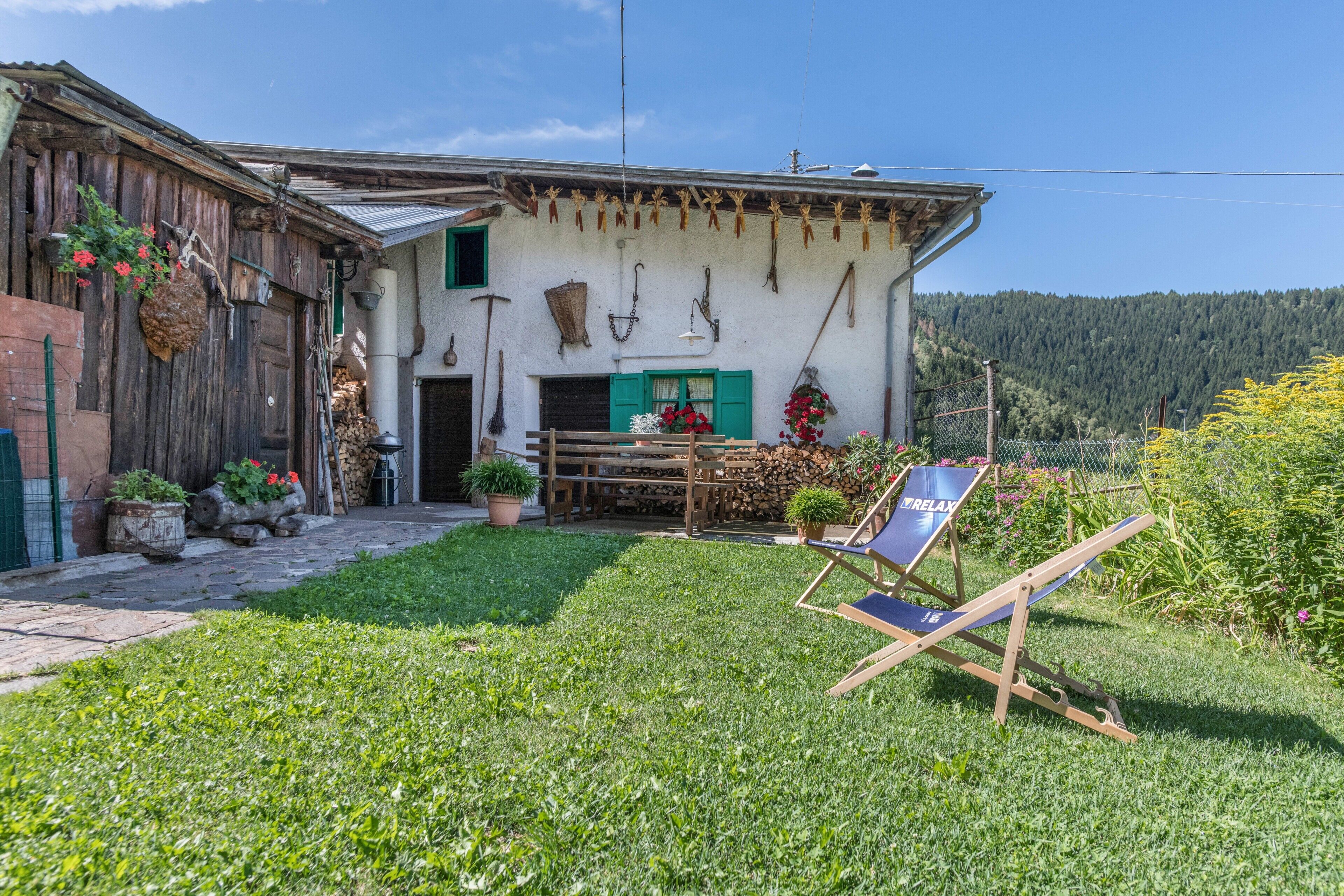 A rustic house with a wooden exterior, a small porch, and a garden area with a chair and potted plants.