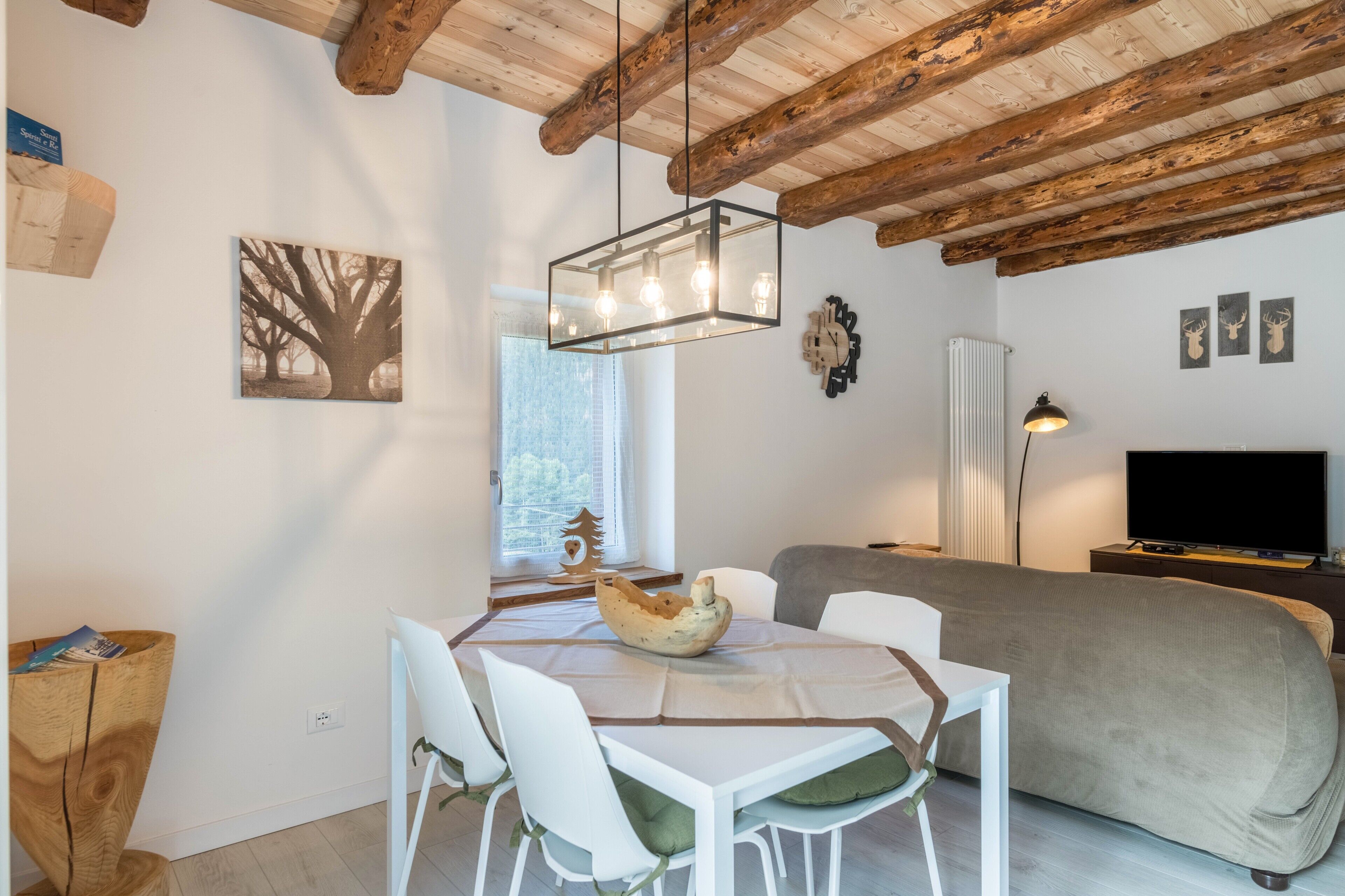 Une pièce moderne avec un plafond en bois, une table à manger avec des chaises, un canapé, un téléviseur et une horloge murale.