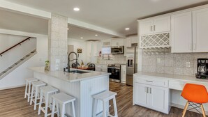 Una cocina moderna con armarios blancos, una isla central con taburetes de bar, un refrigerador de acero inoxidable y un microondas.