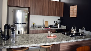 A modern kitchen with a stainless steel refrigerator, granite countertop, wooden cabinets, and a kitchen island with stools.