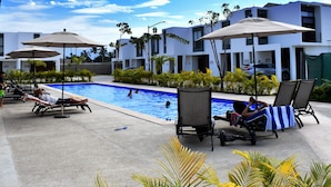 A poolside area with lounge chairs, umbrellas, and a swimming pool.