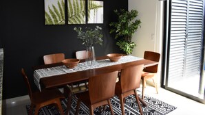A dining area with a wooden table, chairs, and a black and white patterned rug. There are three framed pictures on the wall above the table.