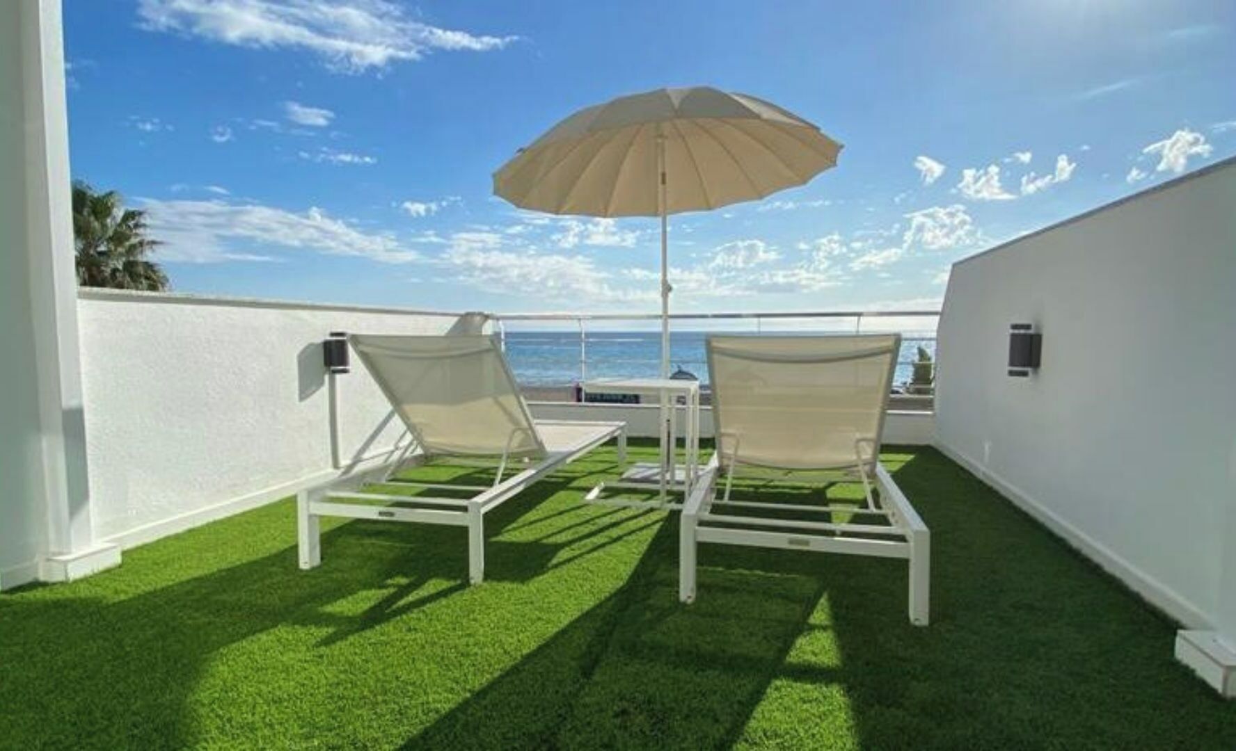 Two lounge chairs with a canopy umbrella on a rooftop terrace with a view of the ocean.