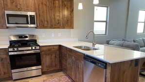 A modern kitchen with wooden cabinets, stainless steel appliances, a built-in dishwasher, and a large island with a sink.
