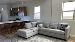 A modern kitchen with a bar area, a gray sectional sofa, and a patterned rug.