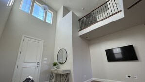 A spacious living room with a high ceiling, a staircase, a mounted TV, and a door.