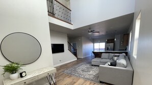 A spacious living area with a grey sofa, a large mirror, and a wooden floor.