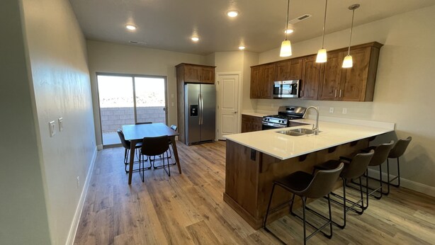 A modern kitchen with wooden cabinets, a stainless steel refrigerator, a built-in oven, and a large island with bar stools.