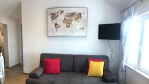 A modern living room with a grey sofa, red and yellow cushions, a world map artwork, a flat-screen TV, and a window with curtains. - Sunone Dubrovnik (Dubrovnik)