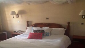 Habitació d'hotel amb un llit gran, un panell de fusta al capçal, dues làmpades laterals i una taula de nit amb una làmpada.
