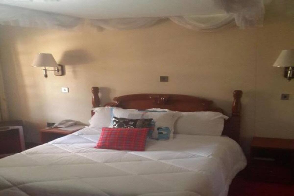 Habitación de hotel con una cama grande, cabecera de madera, dos lámparas de noche y una mesita de noche con lámpara.