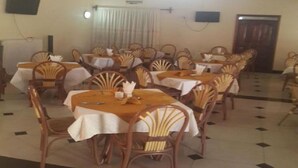 Una zona de dinar amb diverses taules i caires, un candelabrum i una porta al fons.