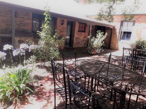 A courtyard with a brick building, metal chairs, and potted plants. - Unwind in Our Cosy 2 BR Spa Cottage with Log Fire. Mintaro Hideaway Carpenter (Mintaro)