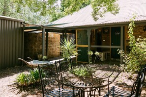 A rustic outdoor seating area with metal chairs and a table, surrounded by greenery and a stone building with a sign reading "LAUNDRY". - Unwind in Our Cosy 2 BR Spa Cottage with Log Fire. Mintaro Hideaway Carpenter (Mintaro)