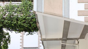 Kapea polku johtaa rakennuksen sisäänkäynnille, jonka yläpuolella on kyltti, jossa lukee ”Tervetuloa”. Polun ympärillä on vihreää kasvillisuutta ja sen vieressä pysäköity ajoneuvo.