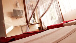 Hotellihuone, jossa on sänky, televisio ja hyttysverkko.