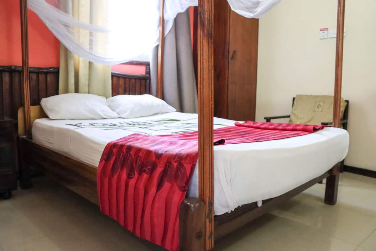 Una cama con dosel con sábanas blancas y una colcha floral roja.