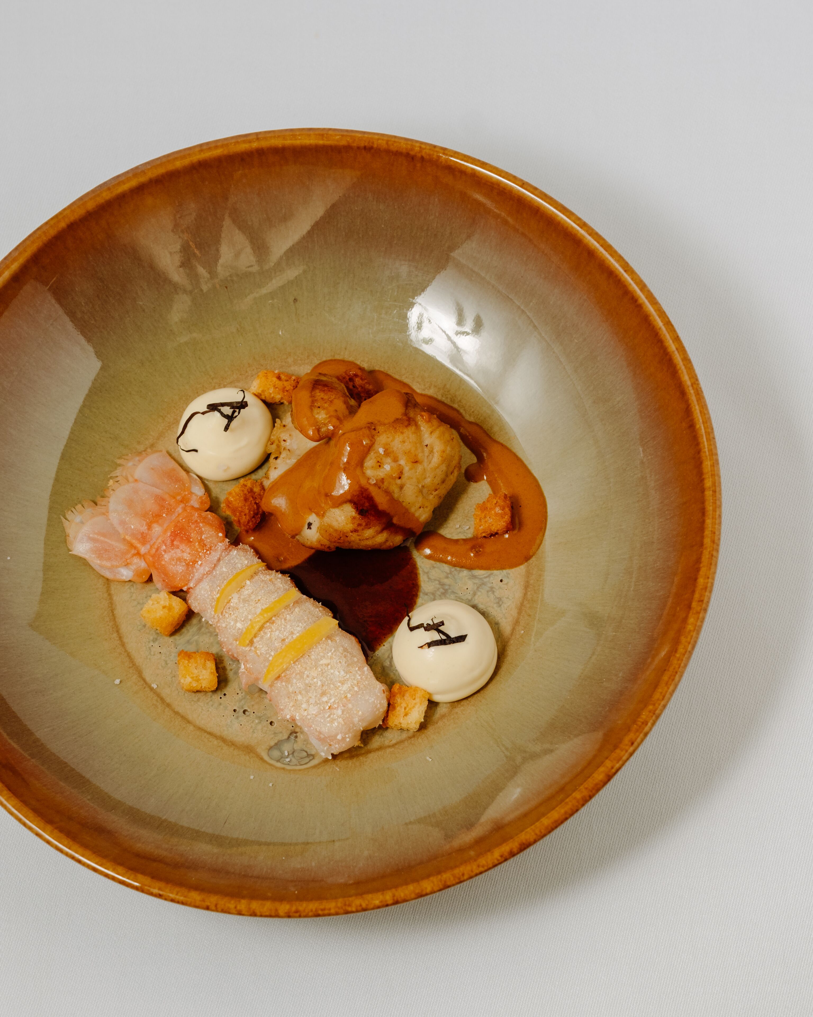 A bowl of food with various items including fish, a sauce, and small round objects.
