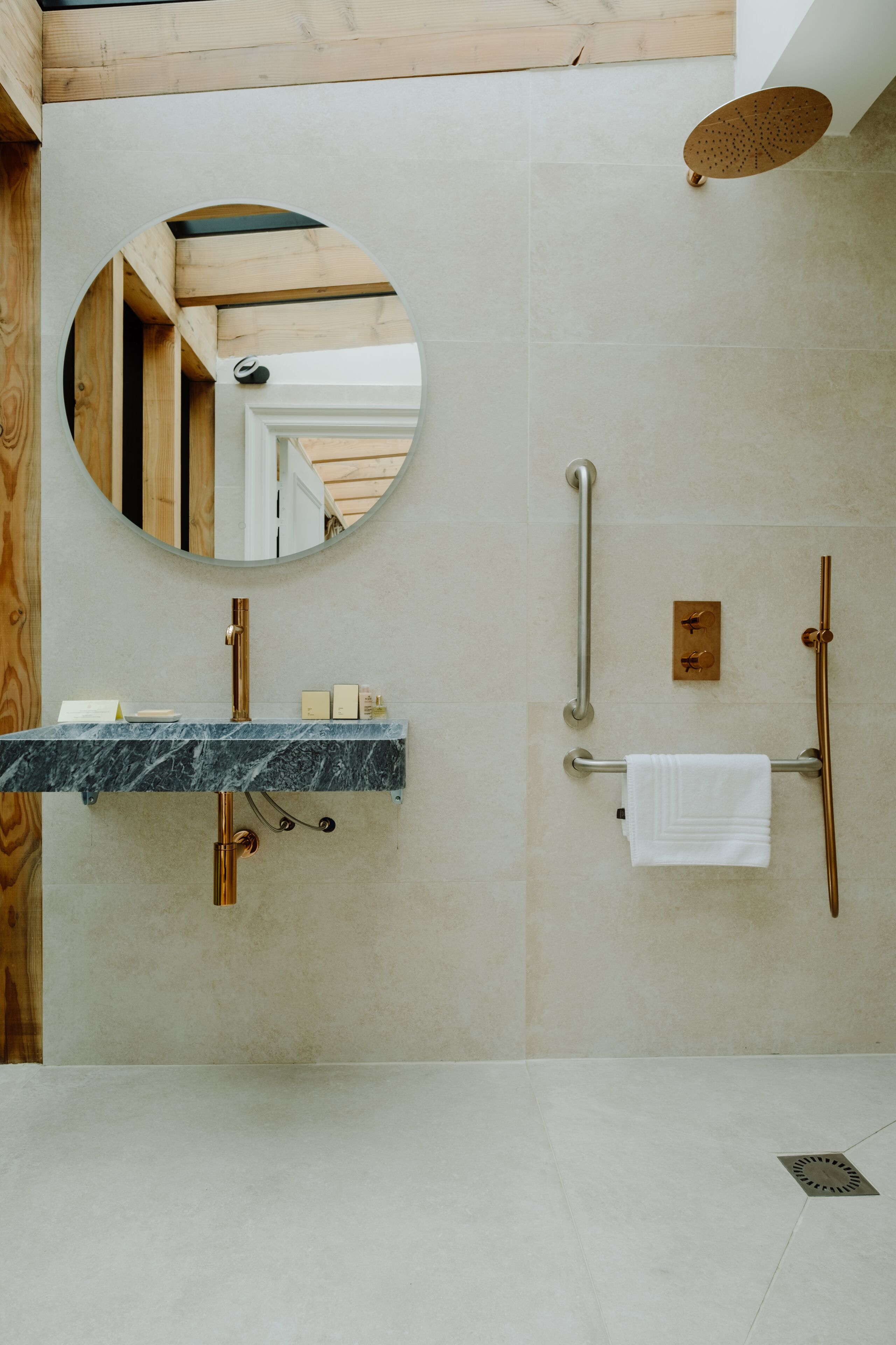 Un baño moderno con lavamanos de mármol, un espejo redondo, un cabezal de ducha de mano y un perchero.