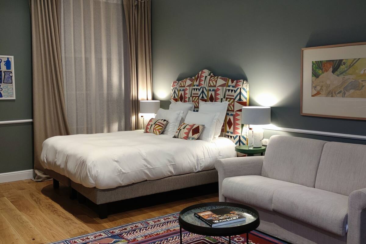 A bedroom with a bed, a sofa, a coffee table, a lamp, and a framed picture on the wall.