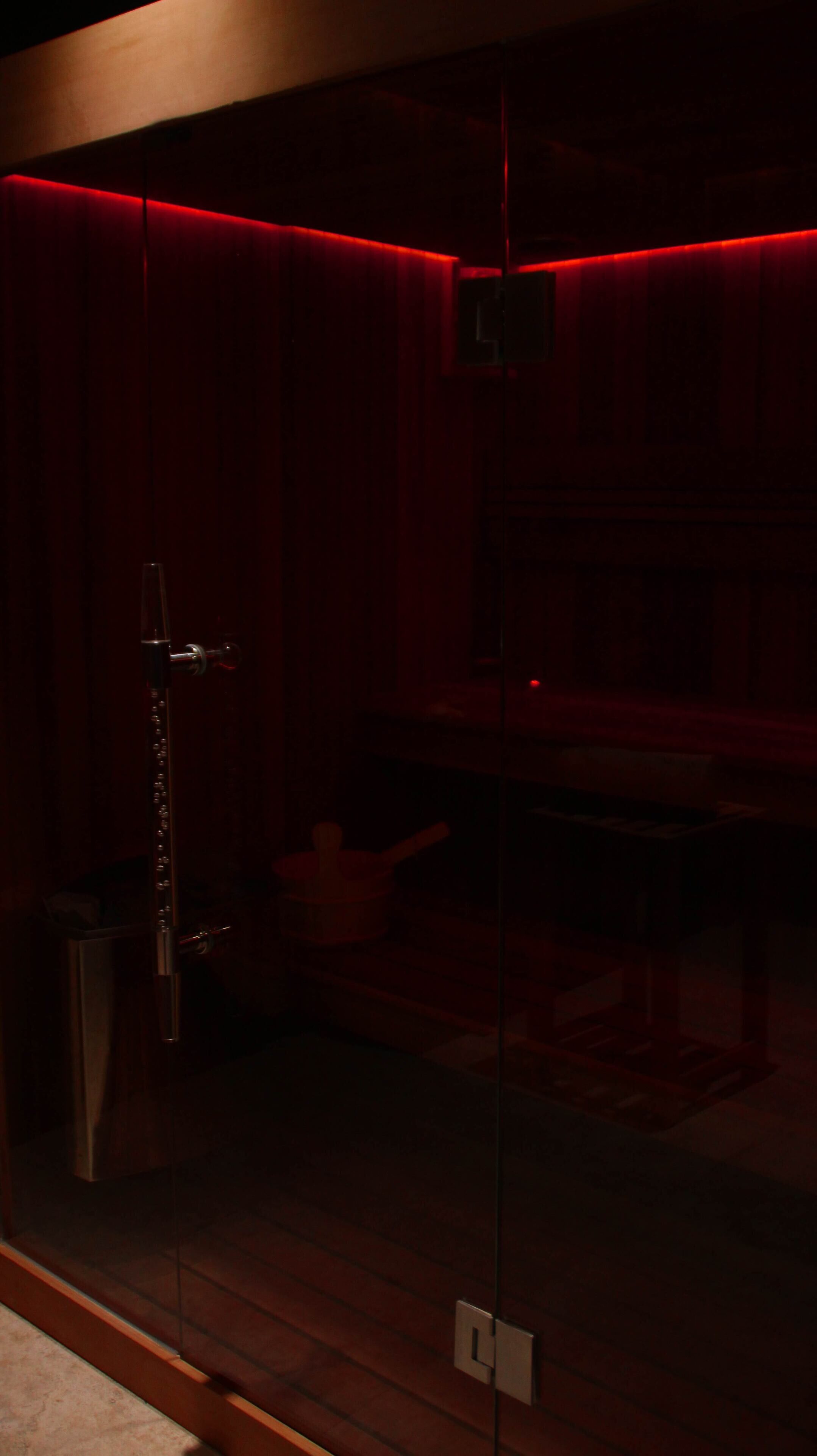 A dimly lit room with a glass partition, a wooden floor, and a red ambient light strip.