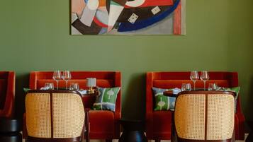 A dining area with a green wall, a colorful abstract painting, and a red sofa set.