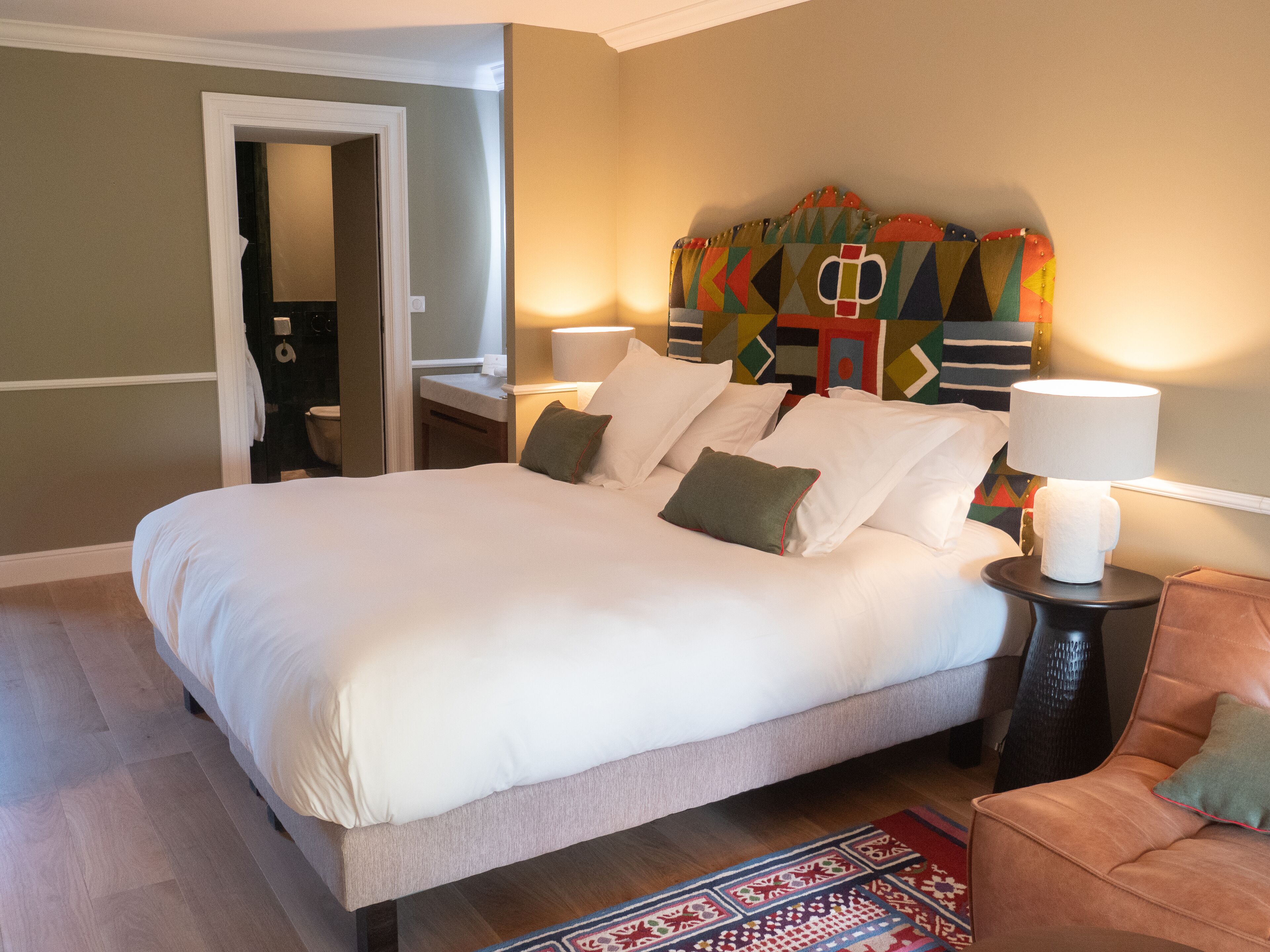 A large bed with white linens, a colorful headboard, bedside lamps, and a patterned rug.
