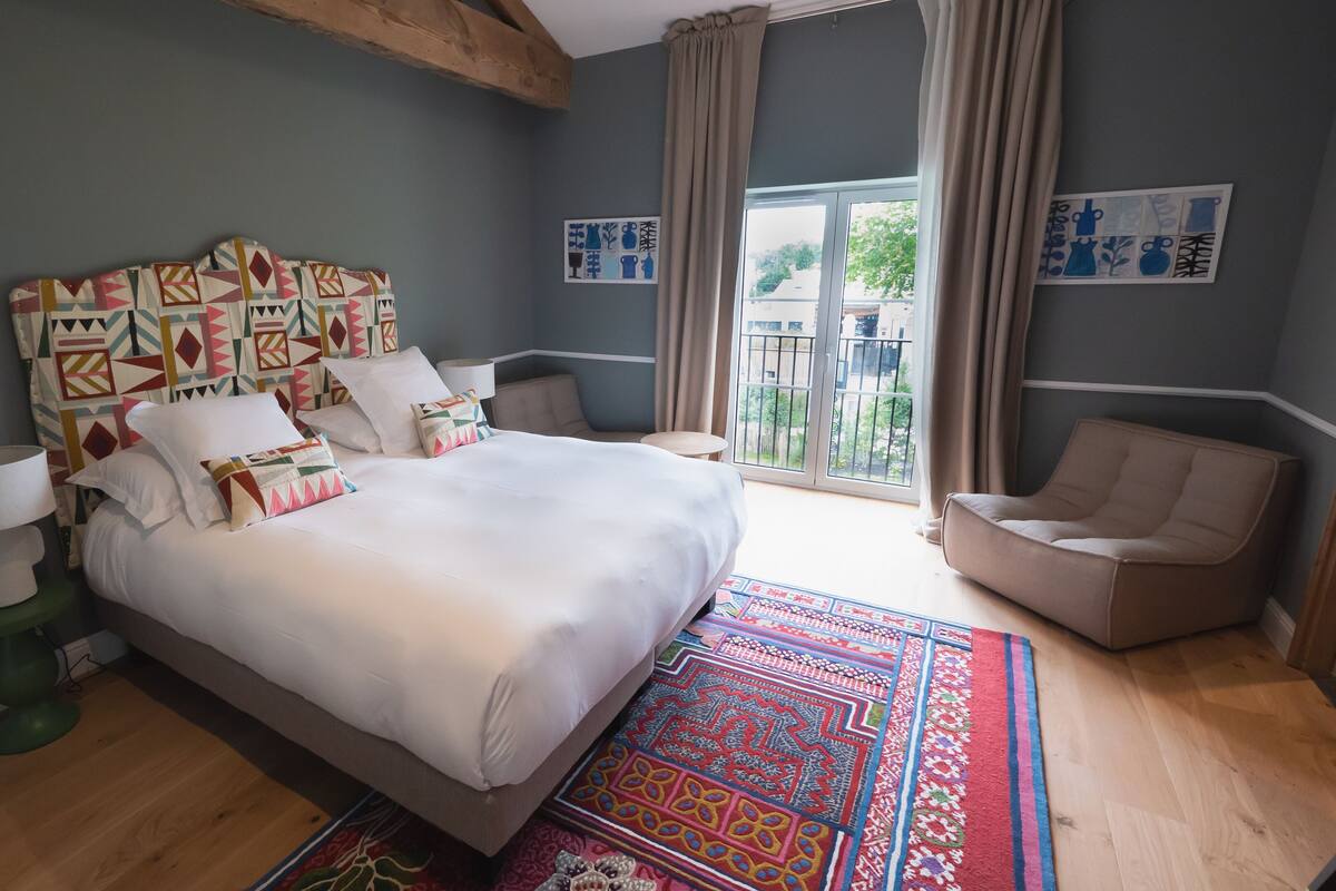 A modern bedroom with a large bed, a green floor lamp, a patterned rug, and a view of the outdoors through a sliding glass door.
