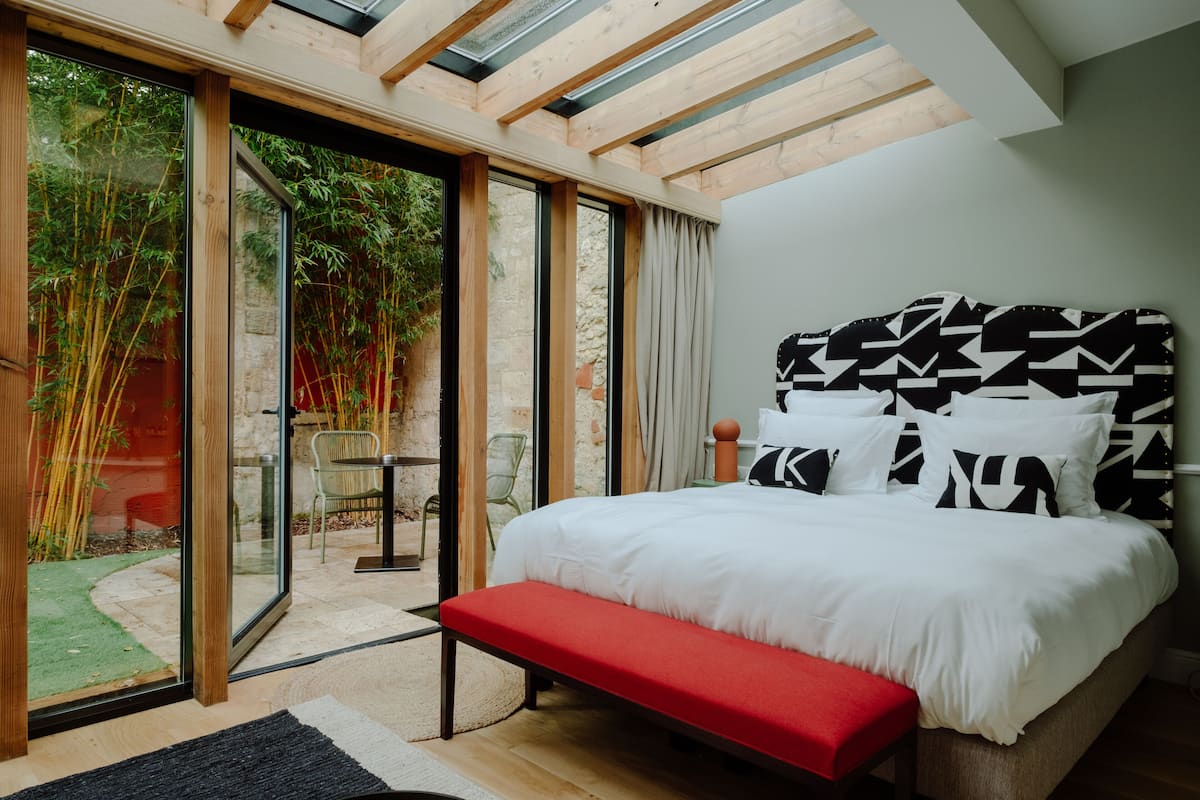 A bedroom with a large bed, a red bench, and a view of a garden through glass doors.