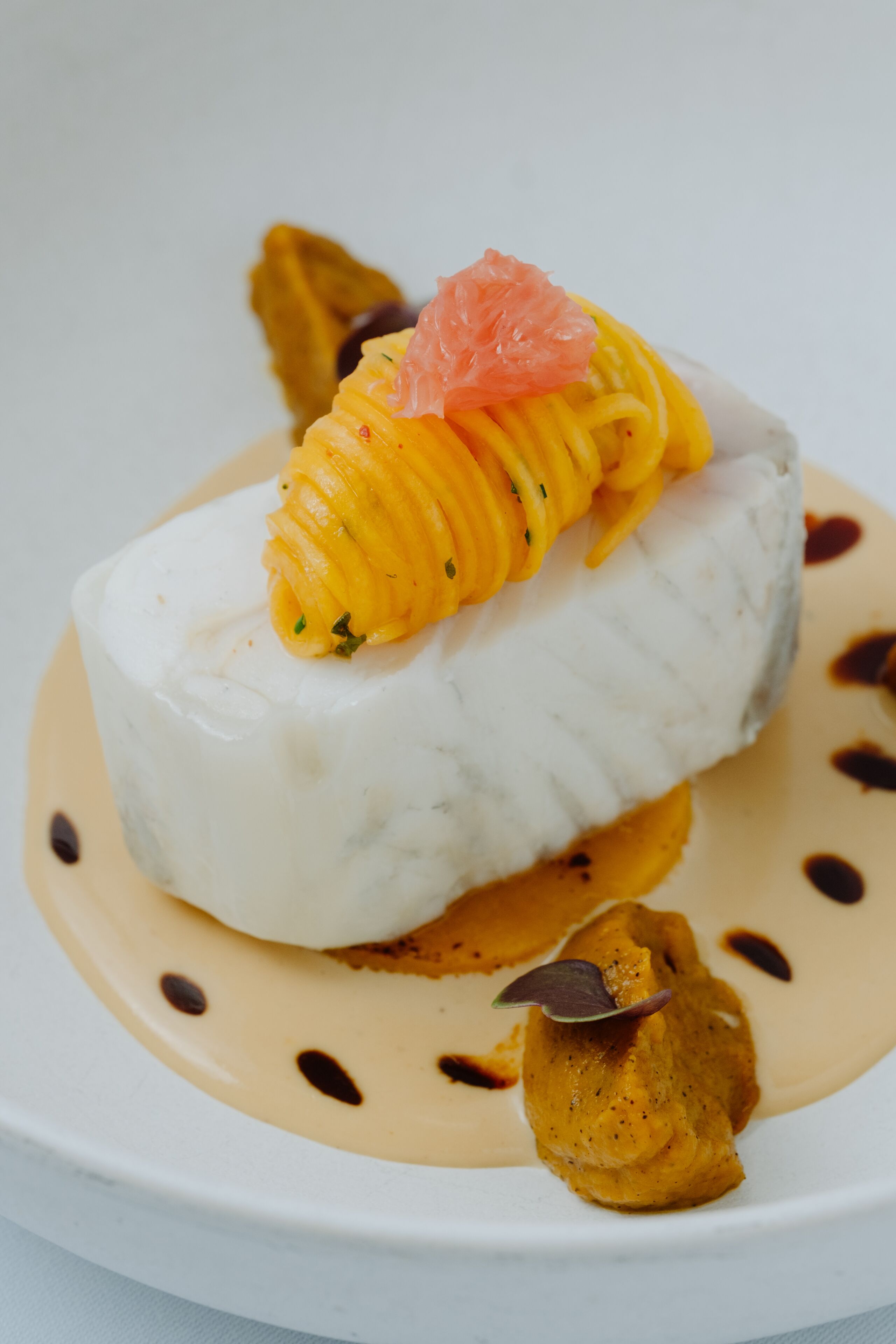 A white plate with a white fish fillet, mango slices, and a garnish on top.