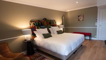 Een keurig opgemaakt slaapkamer met een groot bed, een nachtkastje met lampen, een stoel en een kleurrijk hoofdeinde.