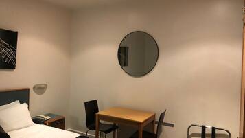 A hotel room with a bed, a desk, two chairs, a mirror, a nightstand, and a wall-mounted lamp.