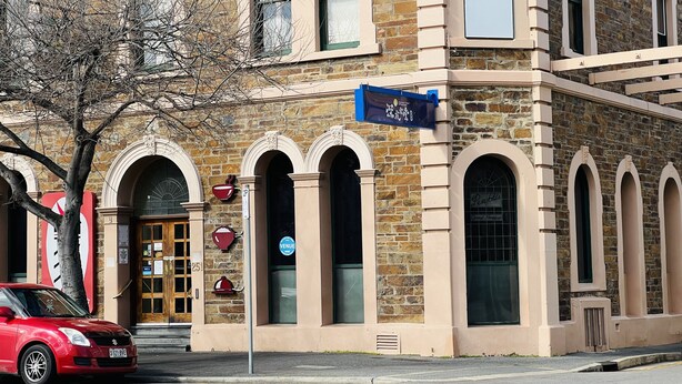 Un bâtiment à la façade en pierre, doté de fenêtres en arc de cercle, et une voiture rouge garée devant.