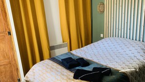 Een slaapkamer met een bed, gordijnen, een houten deur, een radiator en een geweven vloerkleed.
