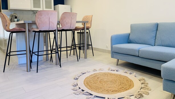 Een moderne keuken met witte kasten, een roestvrijstalen afzuigkap en een eethoek met vier roze stoelen.