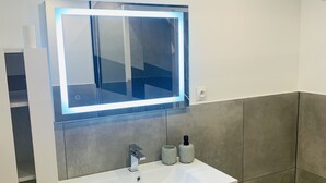 Een moderne badkamer met een wit wastafel, een spiegel met achtergrondverlichting, een toilet en een kastje.