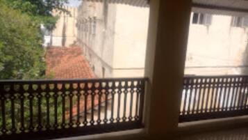 A balcony with a metal railing overlooking a building with a tiled roof and a tree in the background.