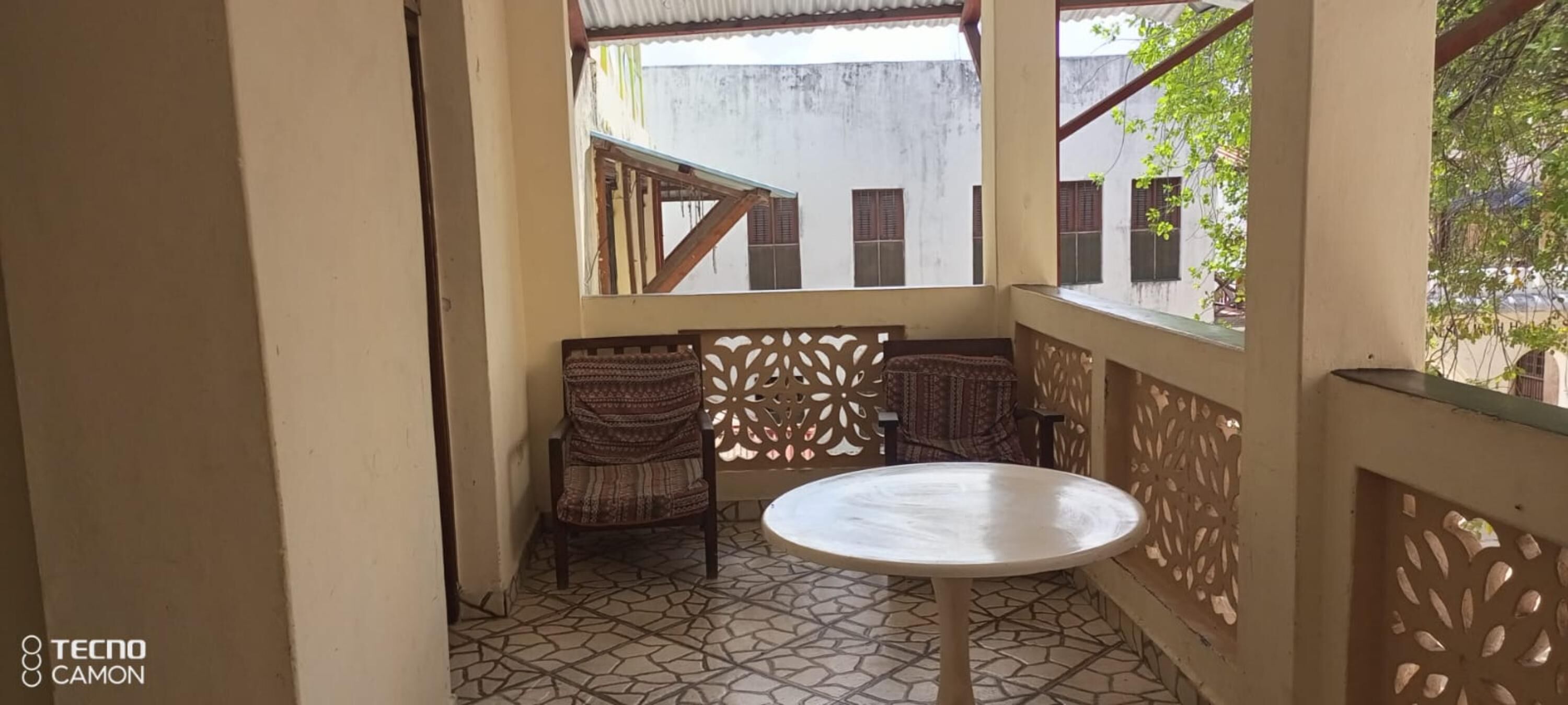 A small, enclosed balcony with a tiled floor, a round table, and two patterned chairs.