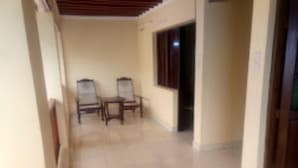 A corridor with two wooden chairs and a small table, leading to a door. - New Mahrus Hotel & Rooftop Restaurant (Lamu)