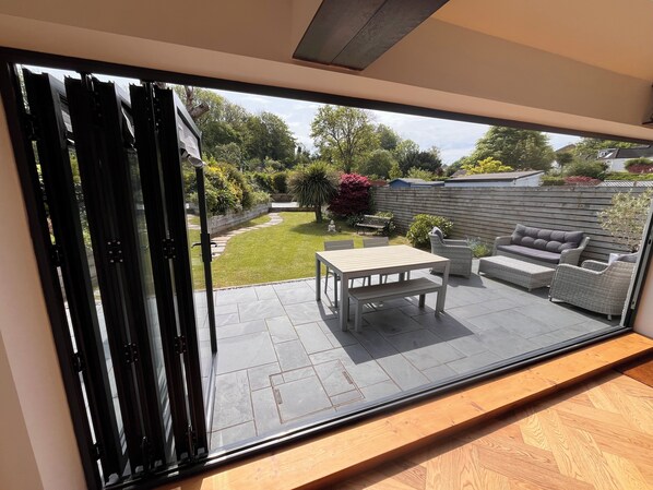 A patio with a table and chairs, a wooden deck, and a garden view.