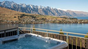 A hot tub with a wooden deck and a view of a lake and mountains. - Castle Cliff Lodge | Spa Pool + Sauna | Games Room (Queenstown)